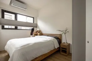 A minimalist bedroom featuring a wooden bed and furniture, with a woman organizing items on the bed.