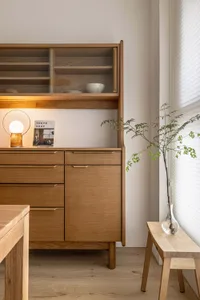 A minimalist interior with a wooden cabinet featuring open shelves and drawers, equipped with modern lighting and a potted pl