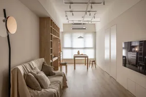 A minimalist living room featuring wood and white decor, with a sofa, floor lamp, and dining area by the window.