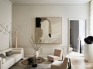 A modern living room with beige furniture, a round glass-top coffee table, and abstract art on the wall.