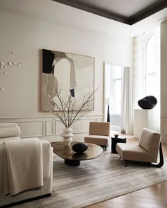 Modern living room with neutral tones, featuring minimalist furniture, abstract art, and a round glass coffee table.