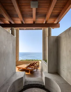Outdoor lounge area with concrete walls, wooden lounge chair, and stone floor.