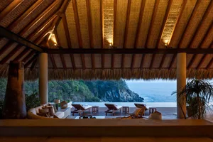 Thatched-roof pavilion overlooking a scenic ocean view with lounge chairs and a swimming pool.
