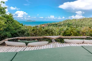 A wooden platform with green cushions overlooking a lush tropical landscape and a clear blue sea with island formations in th