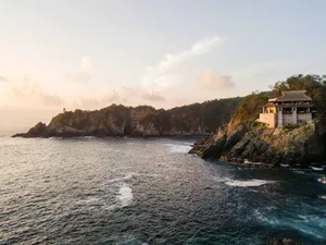 A vacation resort nestled on a rocky cliff overlooking the ocean during sunset.