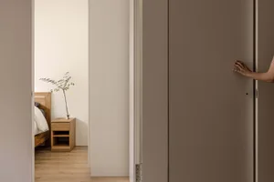 A minimalist bedroom with a white floor, wooden bed, and glass side table.
