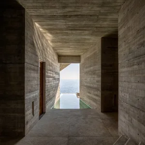 A modern interior with a concrete wall revealing a scenic ocean view.