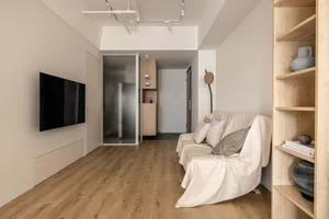 A modern living room with a white couch, wooden shelves, and a large screen TV mounted on the wall.