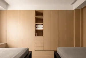 A modern minimalist bedroom with wooden paneling, featuring two beds and a built-in wardrobe.