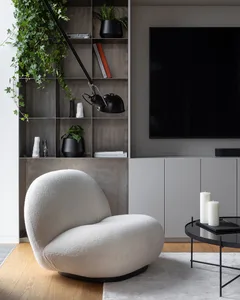 A sleek, white, textured-fabric accent chair in a minimalist living room with a modern design, featuring a black shelving uni
