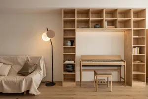 A minimalist living room with wooden shelves and a piano, featuring a sofa and floor lamp.