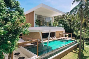 Modern residential villa with a swimming pool surrounded by palm trees, featuring glass and concrete exterior walls and woode