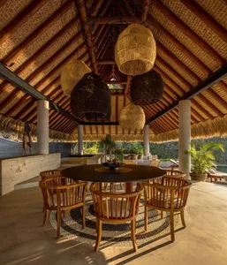 A wooden lounge area with a round table and hanging woven lanterns.