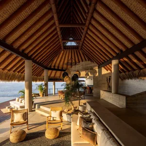 A modern living room with wooden beams on the ceiling and walls, natural light, and comfortable furnishings.