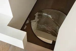 A broken circular mirror on a hardwood floor in a minimalist house.