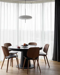 A modern minimalist dining room featuring a wooden table with black legs, four wooden chairs with black seats, and a round ta