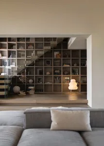 A modern living room featuring a wooden bookshelf with books and decorative items.