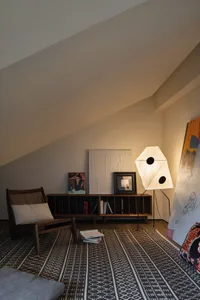 A cozy living room with a wooden armchair, a paper lamp, and a geometric patterned rug.