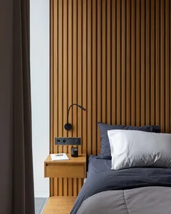 A minimalist bedroom with wooden paneling, a grey bedspread, and a small wooden bedside table with a book and a glass of wate