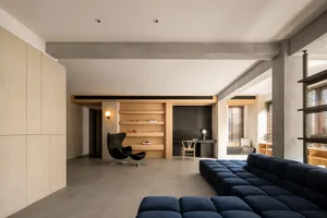 A modern living space featuring exposed concrete walls and window blinds.