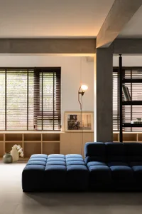 A modern minimalist living room with a blue tufted bench and a wooden shelf with books and a vase of flowers.