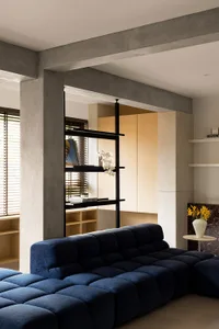 A modern living room featuring a blue modular sofa, concrete pillars, and a minimalist bookshelf.