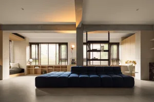A minimalist living room featuring a navy-blue modular sofa, concrete flooring, and large windows with wooden blinds.