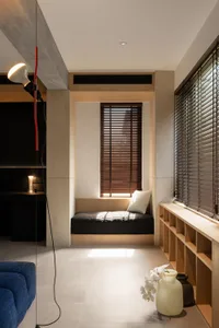 A minimalist window seat with wooden blinds and a white pillow, set against a light-colored wall and floor.