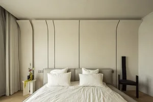 Neutral taupe fabric bed with white pillows, minimalist design, natural light in a bedroom setting.