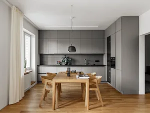 Modern minimalist kitchen with wooden dining table, grey cabinets, and steel accents.