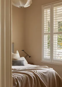 Minimalist bedroom featuring a bed with a lamp and window shutters.