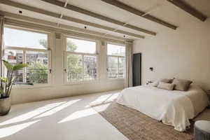 A minimalist bedroom with light-colored wood flooring, white walls, and large windows.