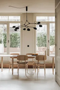 A minimalist dining room with wooden furniture, large windows, and a modern chandelier hanging above the table.