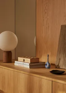 A minimalist interior featuring a wooden cabinet with books, a globe lamp, and decorative objects on top.