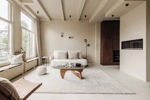 A minimalist living room with a white sofa, a glass coffee table, and a large window letting in natural light.