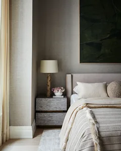 Modern bedroom with neutral textiles and a wooden nightstand with a table lamp and flowers.