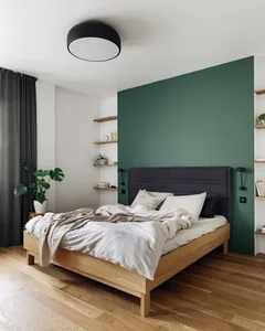 A modern bedroom with a wooden bed frame, green accent wall, and gray curtains.