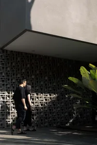 Two people walking past a modern black and white building with a lattice wall and greenery in the foreground.