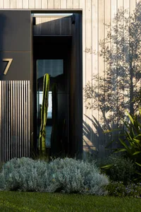 Modern entrance with concrete wall, large glass door, and cactus plant in front of a wooden building.