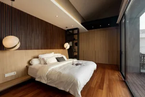 Modern minimalist bedroom with white bedding, wood-paneled walls, and floor-to-ceiling windows.