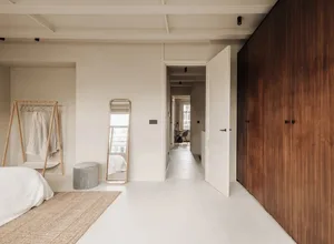 A minimalist bedroom with white walls, a white bed, and wooden closet doors.