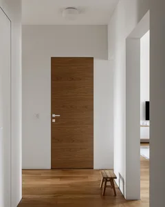 A minimalist private room featuring a wooden door with a white circular light fixture above and a wooden bench in front of th