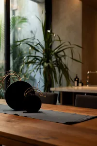 A modern table setting featuring a wooden table and a decorative black vase with dried branches.