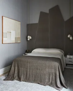 A minimalist bedroom with gray textiles, a bed, and a large abstract painting on the wall.