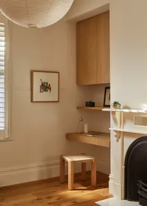 A minimalist home office featuring a wooden desk, shelves, and a stool under a pendant lamp, with a warm, cozy atmosphere.
