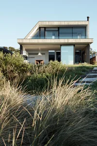 A modern house with a concrete and glass exterior, featuring a sleek, two-story design with large windows and a minimalist ae