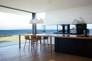 Modern kitchen with wooden table, glass pendant lights, and ocean view.