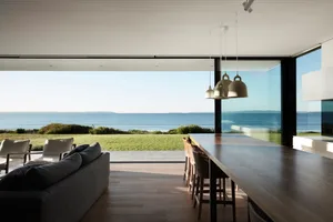 A modern living space featuring wood flooring, large glass windows, and a sleek metal dining table.