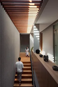 A modern minimalist hallway with wooden stairs and flooring, featuring a woman sitting on the stairs.