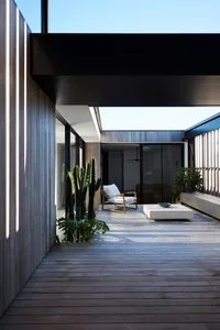 Modern minimalist house exterior terrace with wooden furniture, glass doors, and a cactus plant in the corner.